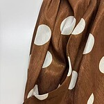 Close-up of brown fabric with large white polka dots, showcasing a smooth texture and elegant design suitable for fashion and apparel.