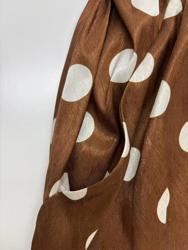 Close-up of brown fabric with large white polka dots, showcasing a smooth texture and elegant design suitable for fashion and apparel.