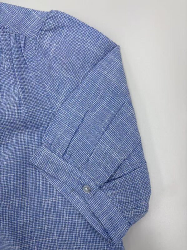 Close-up of a men's blue checkered dress shirt with buttoned sleeve and collar detail, suitable for formal or business wear.