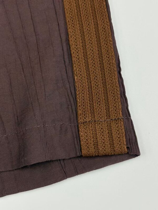 Close-up of traditional brown fabric with orange woven border, showcasing intricate textile craftsmanship and vibrant color contrast.