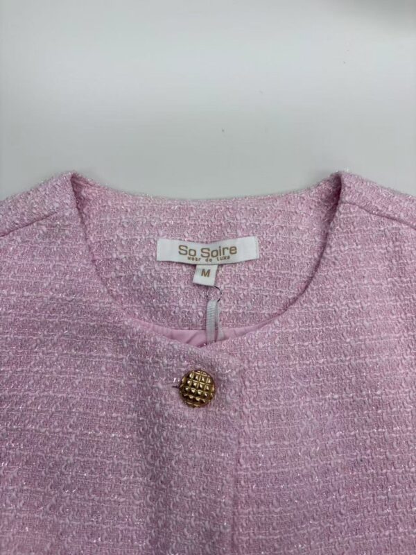 Close-up of a pink tweed women's jacket with a gold button, showcasing elegant fashion suitable for stylish occasions.