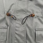 Close-up of a light grey outdoor jacket featuring a drawcord with a toggle for adjustable fit and two front pockets, suitable for outdoor activities.