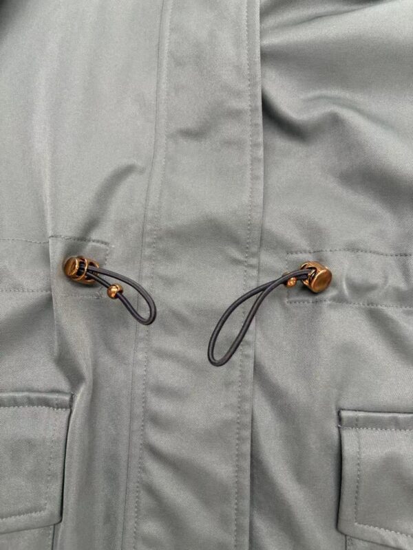 Close-up of a light grey outdoor jacket featuring a drawcord with a toggle for adjustable fit and two front pockets, suitable for outdoor activities.