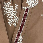 Close-up of a brown jacket with intricate white embroidery and a decorative zipper, showcasing craftsmanship and stylish design.