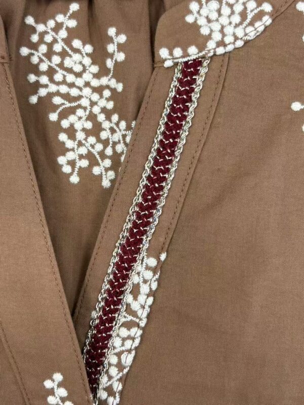 Close-up of a brown jacket with intricate white embroidery and a decorative zipper, showcasing craftsmanship and stylish design.