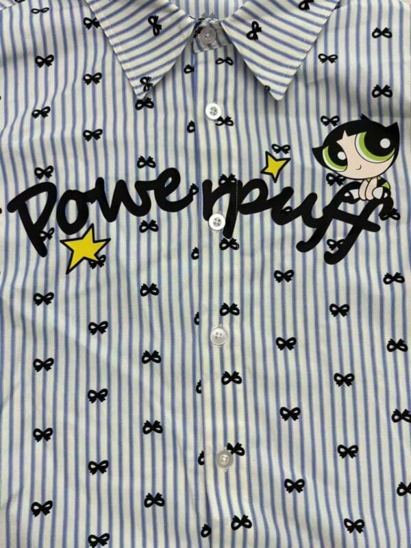 Close-up of a blue and white striped shirt featuring Powerpuff Girls character and logo, with small bow patterns and a playful design.