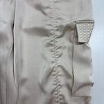 Close-up of a beige dress featuring a decorative pocket with pearl embellishments, showcasing stylish and sophisticated fashion design.
