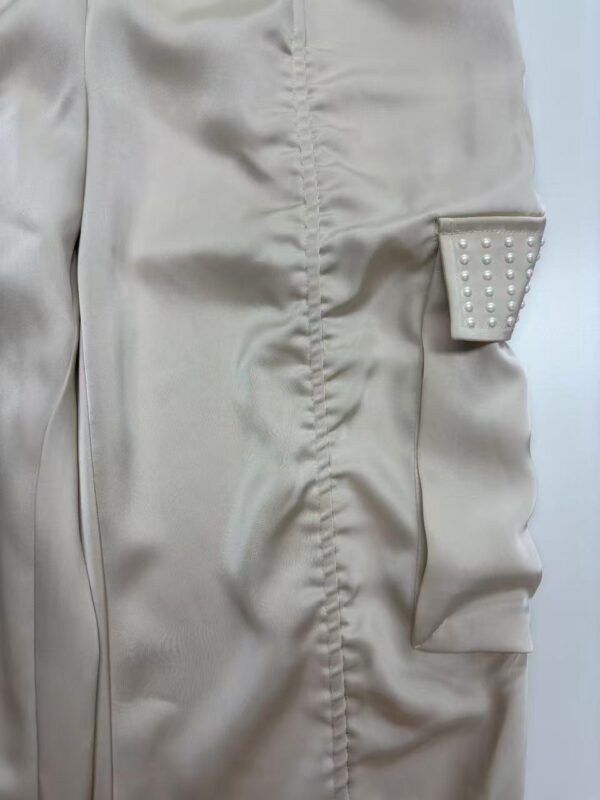 Close-up of a beige dress featuring a decorative pocket with pearl embellishments, showcasing stylish and sophisticated fashion design.
