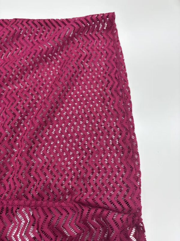 Close-up of vibrant pink lace fabric with intricate zigzag and floral patterns, ideal for stylish clothing and accessories.