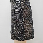 Close-up of a women's skirt with intricate sequin embroidery in black, gold, and silver, showcasing detailed craftsmanship and luxurious fabric.