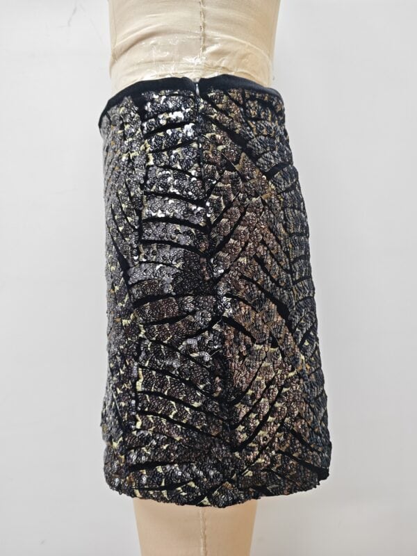 Close-up of a women's skirt with intricate sequin embroidery in black, gold, and silver, showcasing detailed craftsmanship and luxurious fabric.