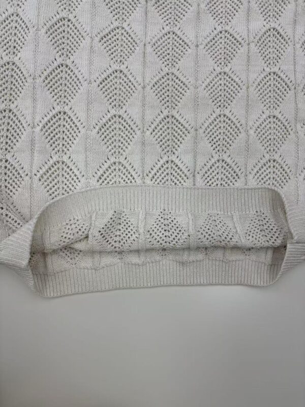 Close-up of a cream-colored knit sweater featuring a detailed geometric pattern and ribbed hem, perfect for stylish winter wear.