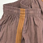 Close-up of casual brown linen pants with yellow stripe detail and elastic waistband, suitable for comfortable everyday wear.