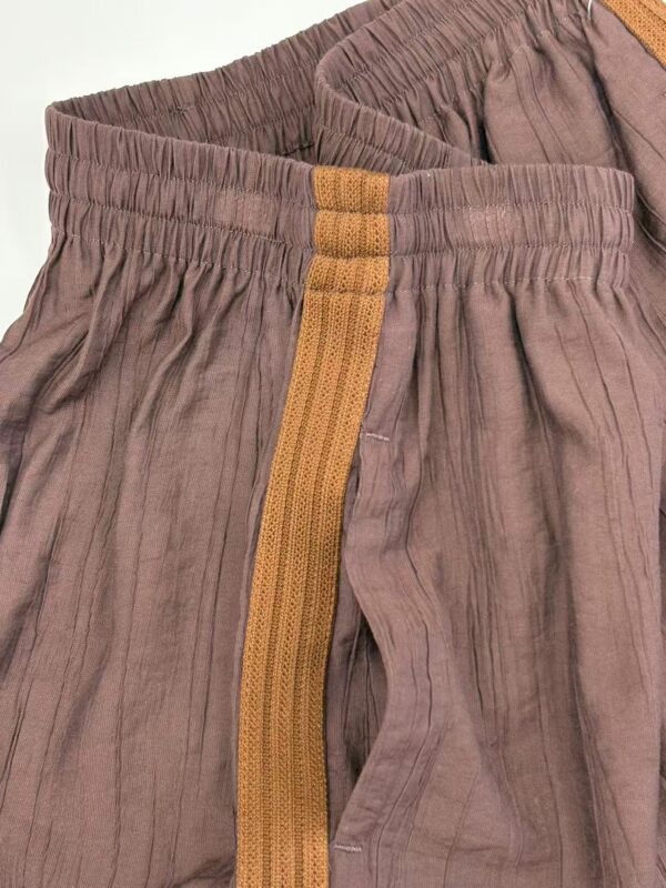 Close-up of casual brown linen pants with yellow stripe detail and elastic waistband, suitable for comfortable everyday wear.