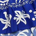 Close-up of vibrant blue fabric with white floral and dotted patterns, showcasing detailed textile design for fashion or home decor.