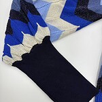 Close-up of a sweater sleeve with a blue, black, and beige argyle pattern and a black cuff, showcasing stylish knitwear design.