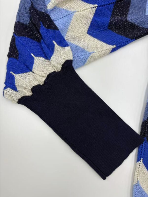 Close-up of a sweater sleeve with a blue, black, and beige argyle pattern and a black cuff, showcasing stylish knitwear design.