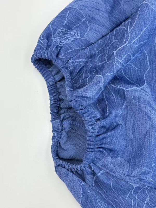 Close-up of a blue fashion garment featuring an elastic cuff and subtle line patterns, highlighting fabric texture and design details.