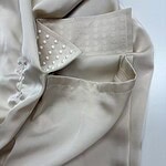 Close-up of a cream-colored blazer featuring pearl embellishments on the lapel and pocket, showcasing sophisticated fashion details.