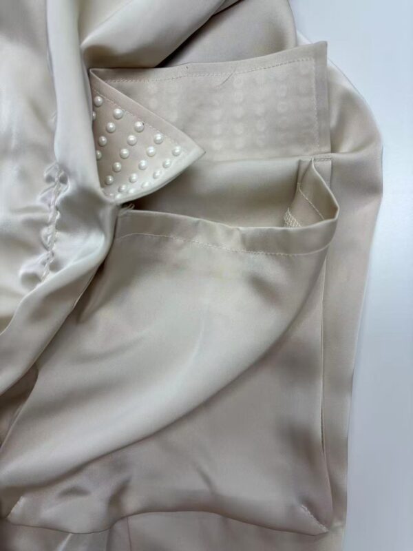 Close-up of a cream-colored blazer featuring pearl embellishments on the lapel and pocket, showcasing sophisticated fashion details.