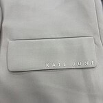 Close-up of a light grey backpack with a front pocket displaying the brand name Kate June in white letters.