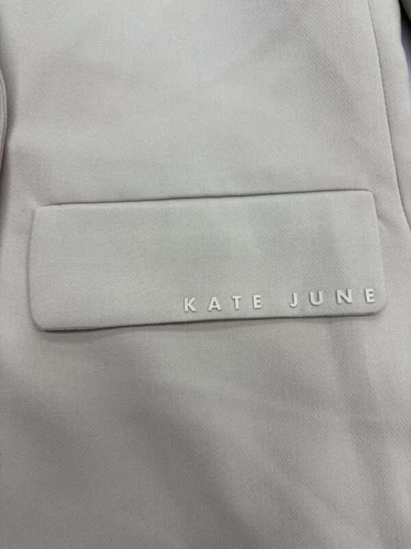 Close-up of a light grey backpack with a front pocket displaying the brand name Kate June in white letters.