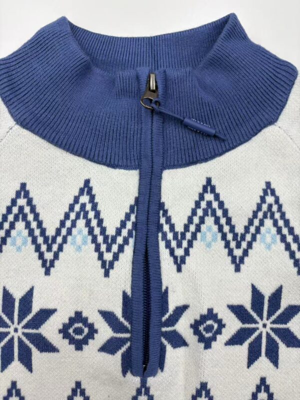 Close-up of a blue and white Nordic pattern sweater with a zipper collar, featuring snowflake and geometric designs, ideal for winter fashion.