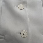 Close-up of a white blazer featuring two stylish buttons and tailored fabric, perfect for professional or formal occasions.