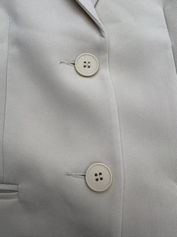 Close-up of a white blazer featuring two stylish buttons and tailored fabric, perfect for professional or formal occasions.