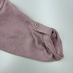 Close-up of a pink knit sweater sleeve with a button and rolled cuff, showcasing soft fabric and casual style.
