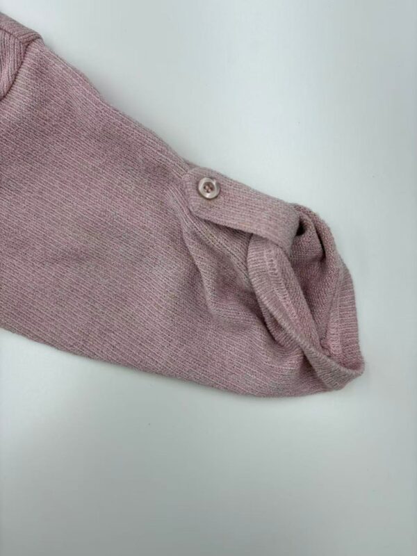 Close-up of a pink knit sweater sleeve with a button and rolled cuff, showcasing soft fabric and casual style.
