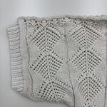Close-up of a beautifully crafted white knitted lace blanket with intricate geometric patterns, perfect for home decor or as a cozy accessory.