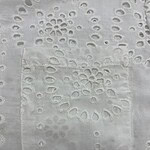 Close-up of white fabric with intricate embroidery and eyelet patterns, showcasing delicate craftsmanship and fine detailing.