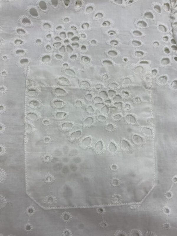 Close-up of white fabric with intricate embroidery and eyelet patterns, showcasing delicate craftsmanship and fine detailing.