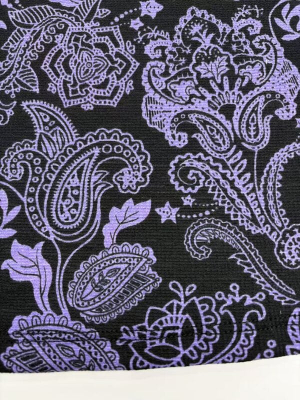 Close-up of a black fabric with intricate purple paisley and floral patterns, showcasing detailed embroidery suitable for fashion and textile design.