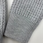 Close-up of a gray knitted sweater sleeve showing textured pattern and ribbed cuff, ideal for fall and winter fashion.