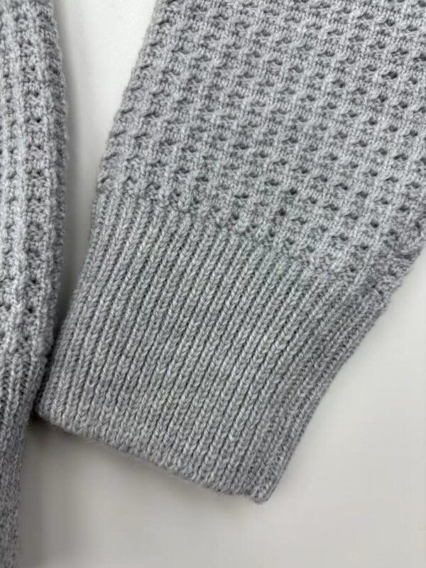 Close-up of a gray knitted sweater sleeve showing textured pattern and ribbed cuff, ideal for fall and winter fashion.