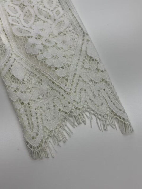 Close-up of intricate white lace fabric with floral patterns and fringed edges, ideal for fashion and wedding dress design.