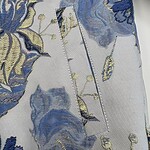 Close-up of luxurious floral fabric with blue, gold, and cream embroidery, showcasing intricate details and high-quality textile craftsmanship.