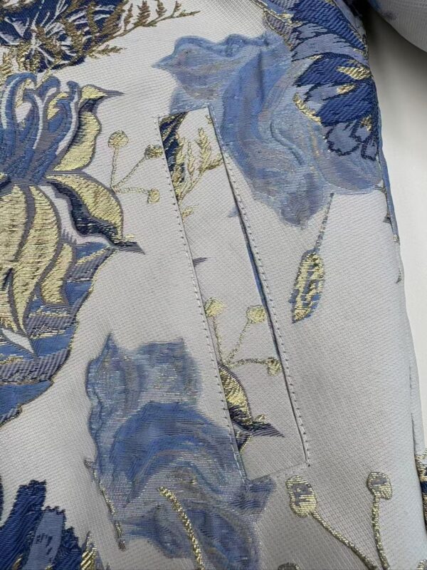 Close-up of luxurious floral fabric with blue, gold, and cream embroidery, showcasing intricate details and high-quality textile craftsmanship.
