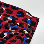 Close-up of a red leopard print shirt with black, white, and blue spots, featuring a buttoned cuff detail.