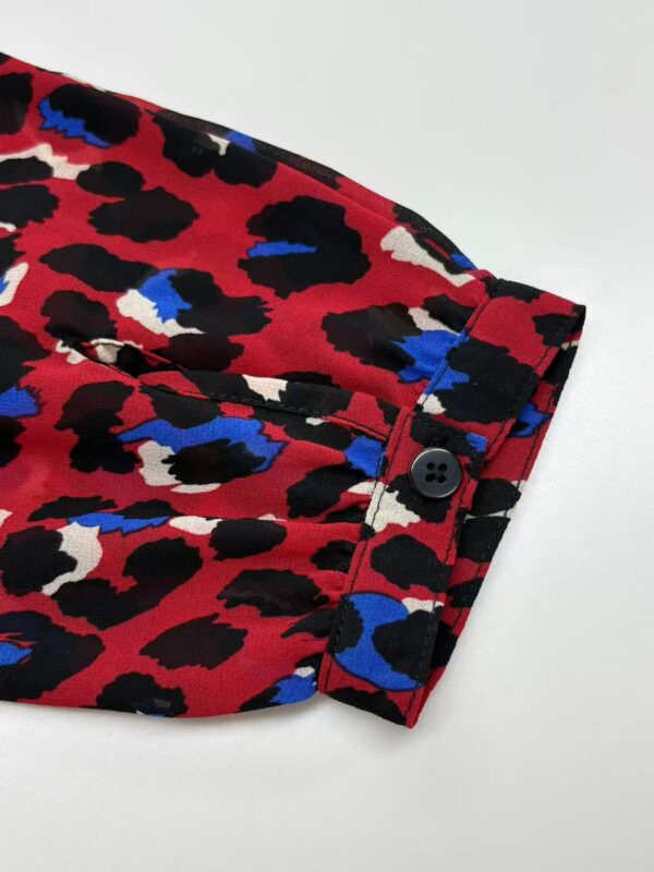 Close-up of a red leopard print shirt with black, white, and blue spots, featuring a buttoned cuff detail.