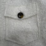 Detailed view of a wool coat's pocket with a single button, showcasing textured fabric and craftsmanship.