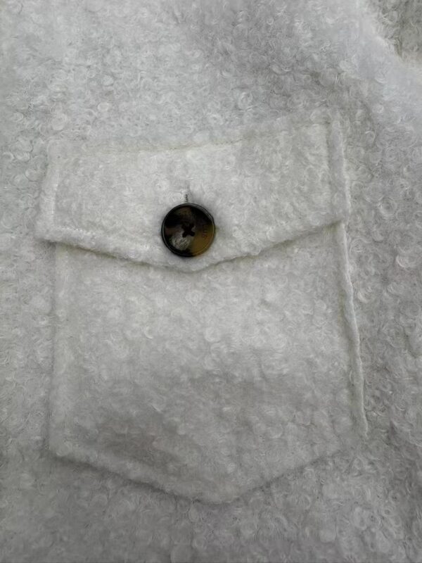 Detailed view of a wool coat's pocket with a single button, showcasing textured fabric and craftsmanship.