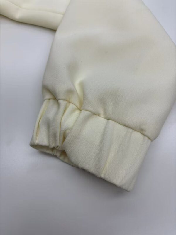 Close-up of a cream-colored fabric sleeve featuring an elastic cuff, showcasing smooth texture and neat stitching, ideal for fashion or clothing product display.