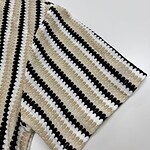 Close-up of a striped knit sweater with black, white, and beige colors, showcasing detailed knitting pattern and texture.