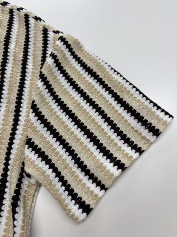 Close-up of a striped knit sweater with black, white, and beige colors, showcasing detailed knitting pattern and texture.