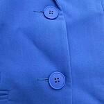 Close-up image of a blue shirt with two matching buttons and detailed stitching, showcasing fabric texture and design.