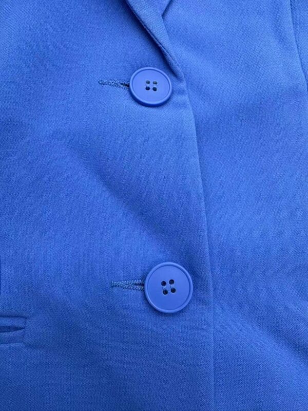 Close-up image of a blue shirt with two matching buttons and detailed stitching, showcasing fabric texture and design.