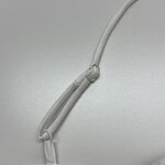 Close-up of a white adjustable strap with a knot, attached to a white fabric surface, possibly part of clothing or bedding.